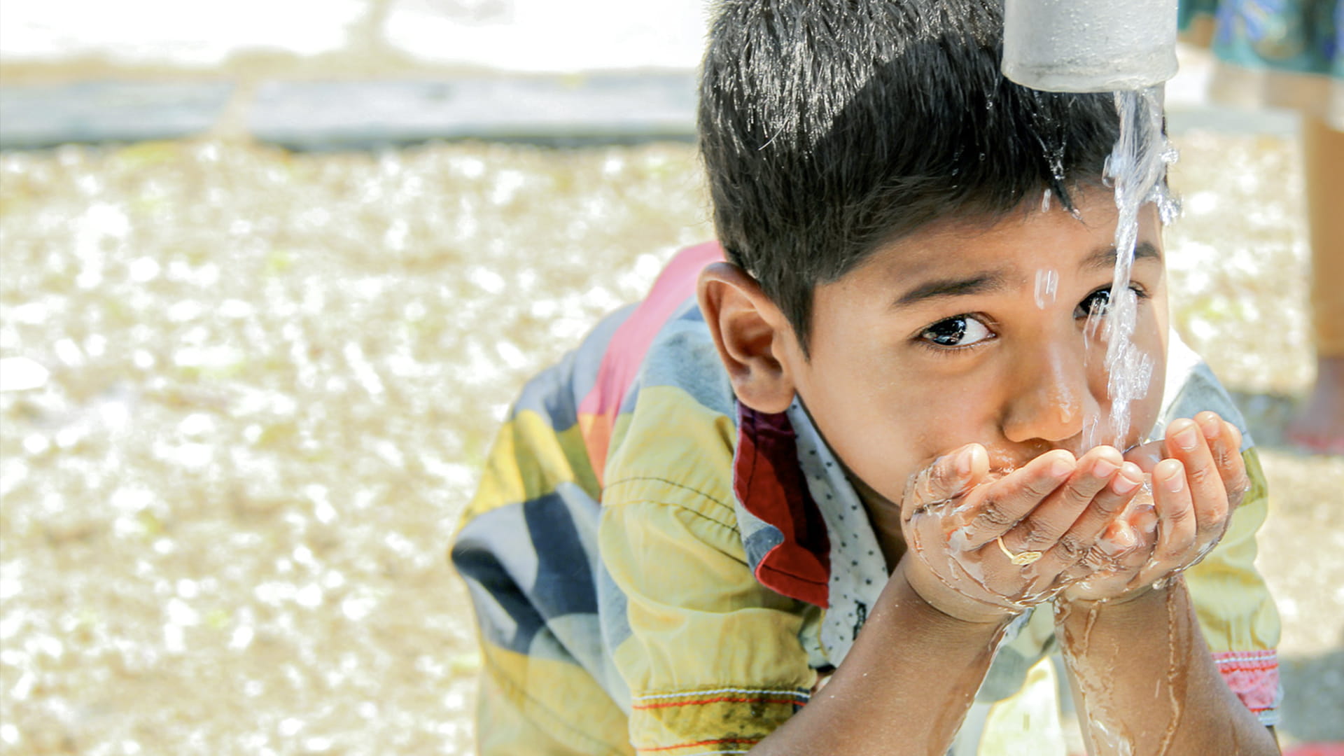 A young boy drinking fresh water from a water well.