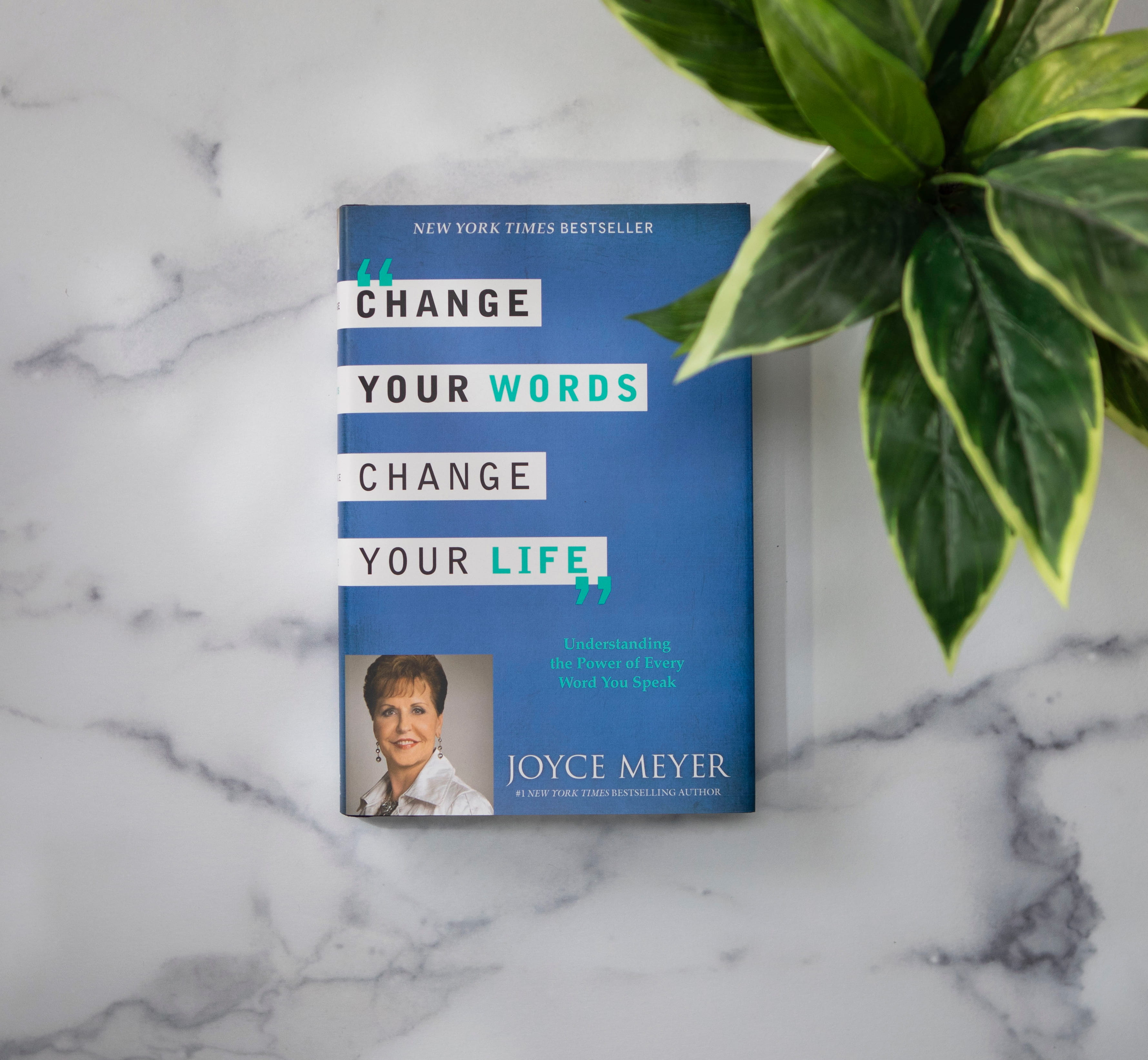 Change Your Words, Change Your Life hardcover book by Joyce Meyer, sitting on a white granite surface with green plant.