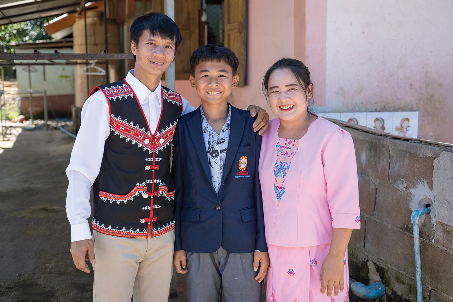 Smiling family standing together outside a home, with parents beside their school-aged son in uniform.
